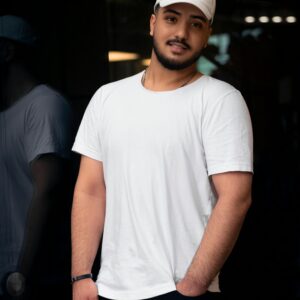 Young man in a white t-shirt and cap smiling and posing against a dark background.
